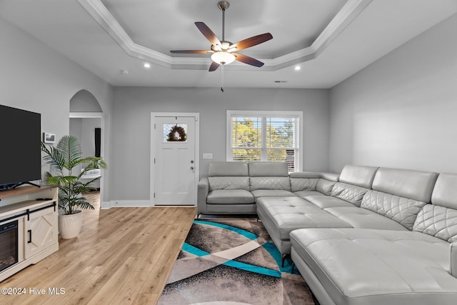 living room featuring a tray ceiling, ceiling fan, crown molding, and light wood-type flooring