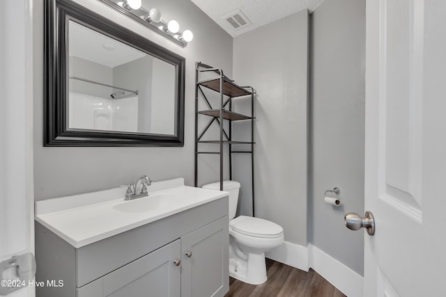 bathroom featuring vanity, a shower, hardwood / wood-style flooring, toilet, and a textured ceiling