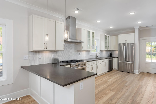 kitchen with decorative light fixtures, stainless steel appliances, white cabinetry, and wall chimney exhaust hood