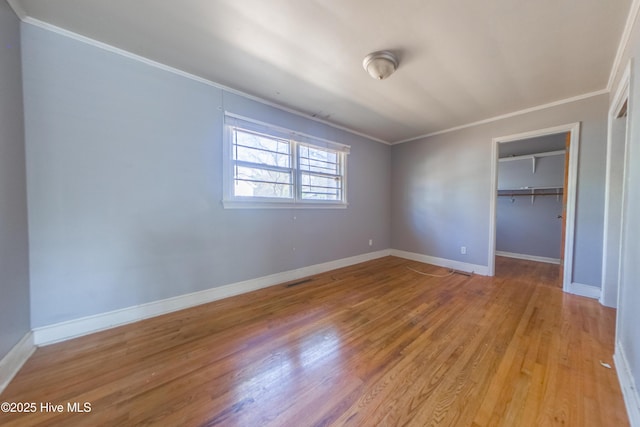 unfurnished bedroom with crown molding, a spacious closet, a closet, and light hardwood / wood-style flooring