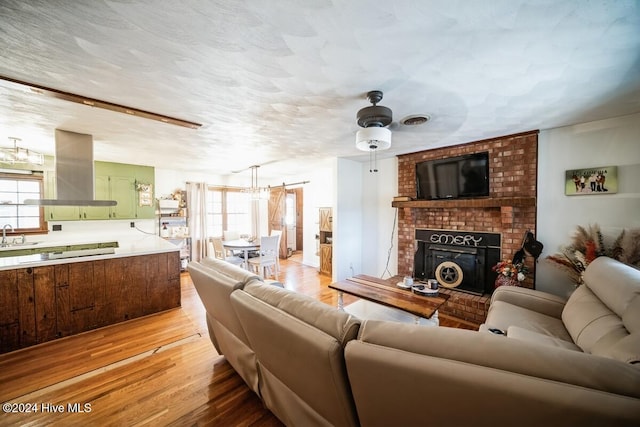 living room featuring ceiling fan, plenty of natural light, a brick fireplace, and light wood-type flooring