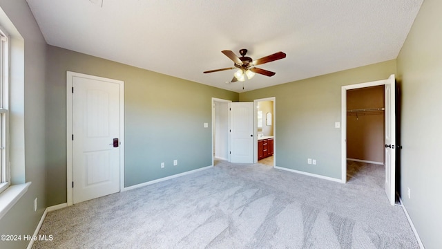 unfurnished bedroom with ceiling fan, ensuite bathroom, a spacious closet, and light carpet