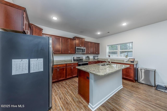 kitchen with light stone countertops, stainless steel appliances, sink, wood-type flooring, and a center island with sink