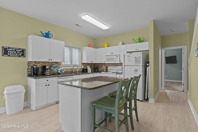 kitchen with backsplash, white appliances, dark stone countertops, white cabinets, and a center island