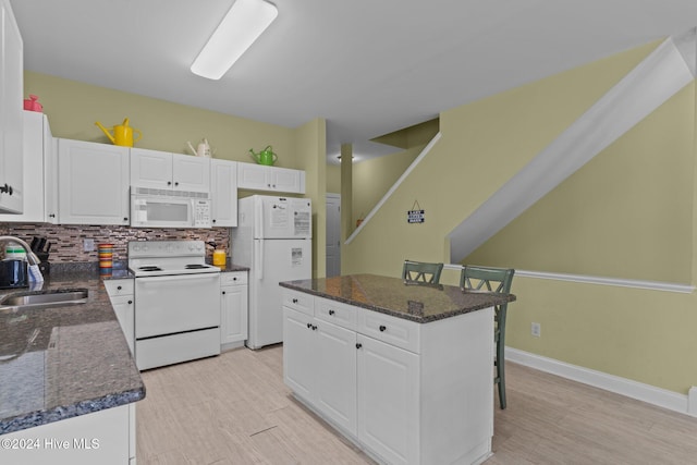 kitchen featuring white cabinets, a kitchen breakfast bar, white appliances, and sink