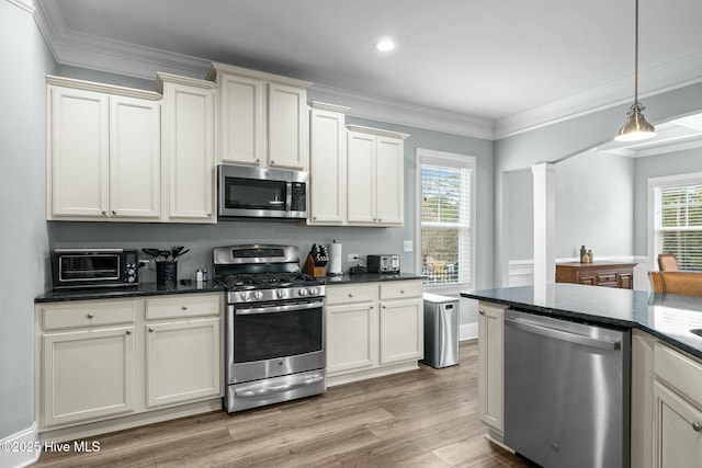 kitchen with decorative light fixtures, cream cabinets, ornate columns, light wood-type flooring, and appliances with stainless steel finishes