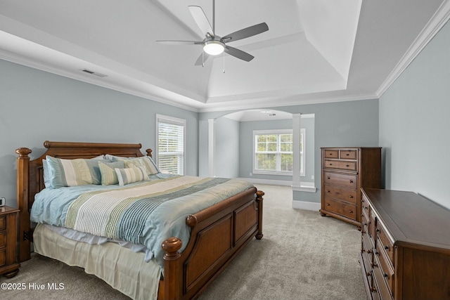 bedroom with a raised ceiling, light colored carpet, ceiling fan, ornamental molding, and decorative columns