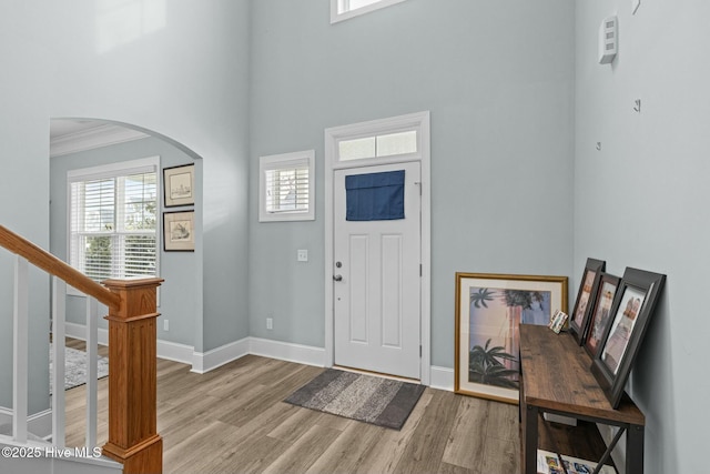 entryway with ornamental molding, light hardwood / wood-style flooring, and a towering ceiling