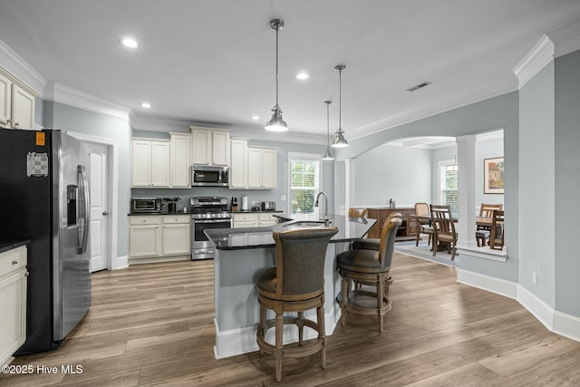 kitchen with decorative light fixtures, a center island with sink, ornate columns, a kitchen bar, and appliances with stainless steel finishes