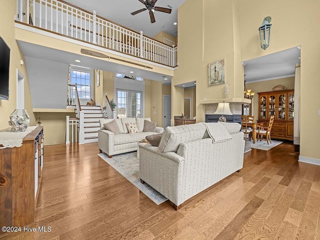 living room featuring ceiling fan, a towering ceiling, wood-type flooring, and ornamental molding