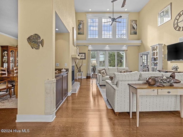 living room featuring ceiling fan, crown molding, wood-type flooring, and a high ceiling