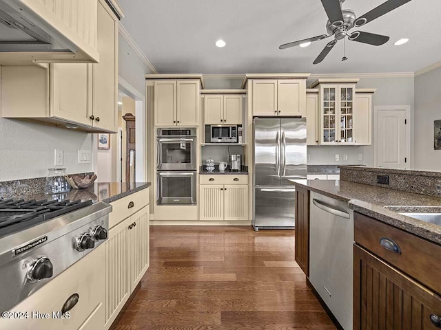 kitchen featuring stainless steel appliances, dark stone countertops, cream cabinets, exhaust hood, and ornamental molding