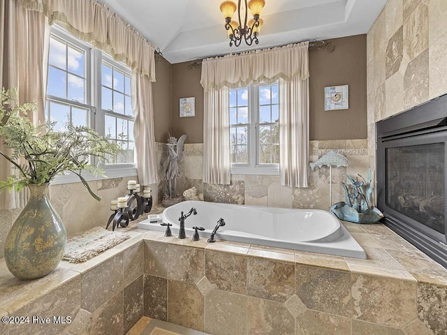 bathroom with vaulted ceiling, a tile fireplace, tiled bath, and a chandelier