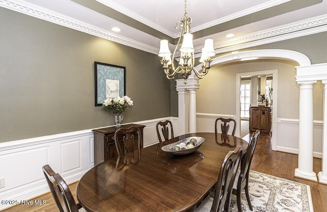 dining space with dark wood-type flooring, an inviting chandelier, ornamental molding, and decorative columns