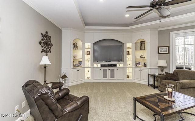 living room featuring built in shelves, ornamental molding, carpet flooring, ceiling fan, and a tray ceiling