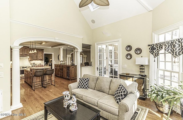 living room with ornate columns, hardwood / wood-style floors, ceiling fan, high vaulted ceiling, and a wealth of natural light