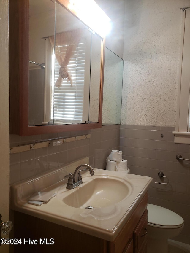 bathroom with vanity, toilet, and tile walls