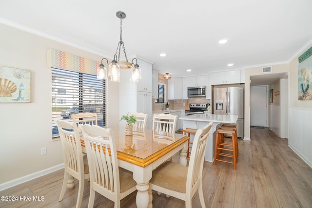 dining room with light wood-type flooring, an inviting chandelier, crown molding, and sink