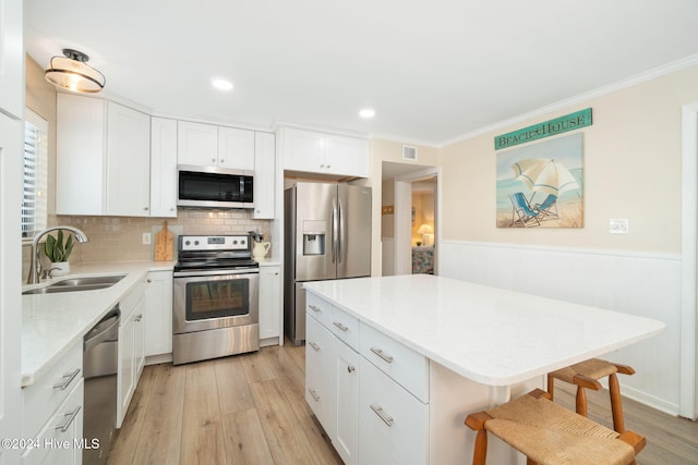 kitchen with sink, stainless steel appliances, a kitchen island, a kitchen breakfast bar, and white cabinets