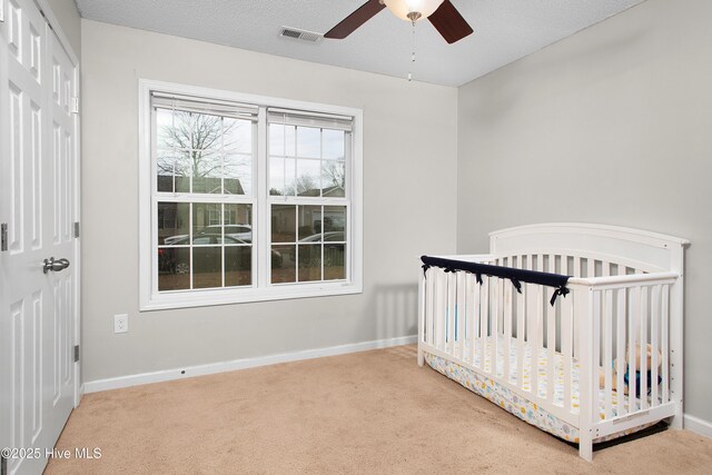 unfurnished bedroom featuring ceiling fan, carpet floors, a nursery area, and a textured ceiling