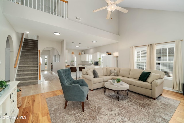 living room featuring light wood-type flooring, a towering ceiling, and ceiling fan