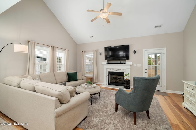 living room featuring ceiling fan, light hardwood / wood-style flooring, a high end fireplace, and high vaulted ceiling