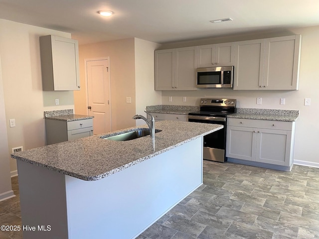 kitchen featuring sink, stainless steel appliances, light stone countertops, and a center island with sink