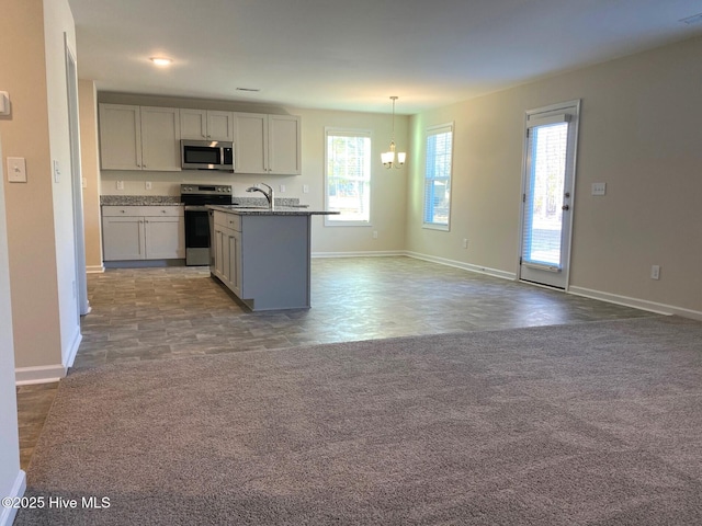 kitchen featuring appliances with stainless steel finishes, hanging light fixtures, light colored carpet, light stone countertops, and a center island with sink