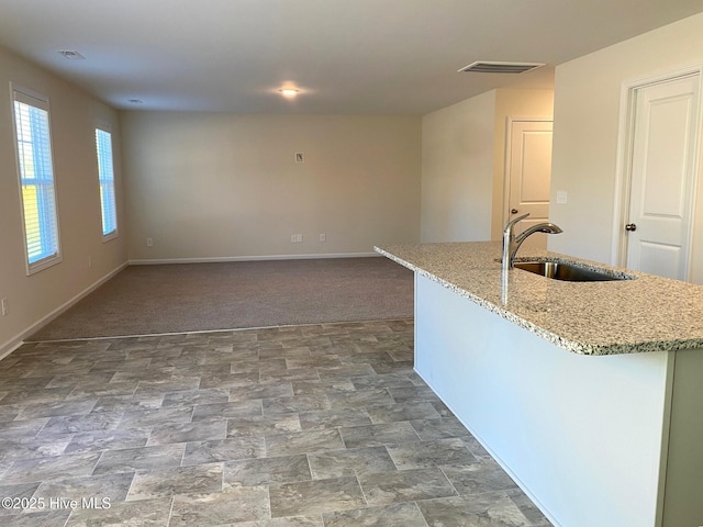 kitchen with a kitchen island with sink, sink, light stone counters, and carpet