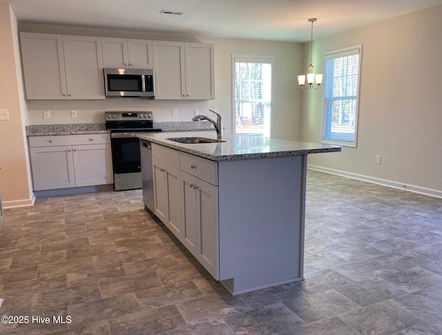 kitchen featuring appliances with stainless steel finishes, sink, hanging light fixtures, light stone countertops, and an inviting chandelier