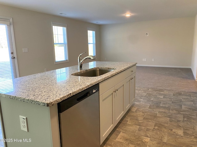 kitchen featuring sink, white cabinets, stainless steel dishwasher, light stone counters, and a center island with sink