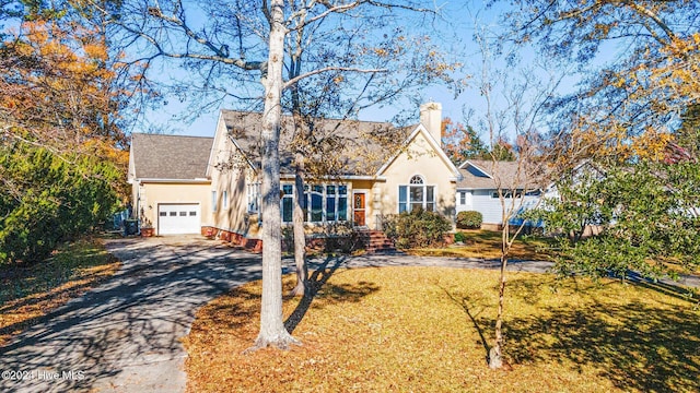 view of front of house featuring aphalt driveway, a garage, a chimney, and stucco siding