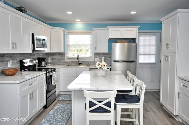 kitchen with a center island, sink, appliances with stainless steel finishes, light stone counters, and a breakfast bar area