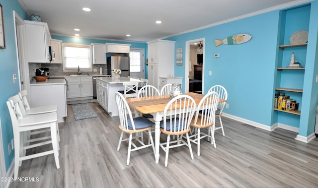 dining space with sink, ornamental molding, and light wood-type flooring