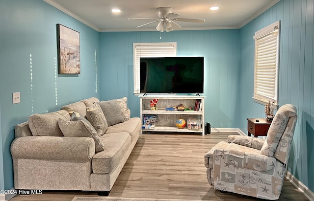 living room featuring ceiling fan, light wood-type flooring, ornamental molding, and wooden walls