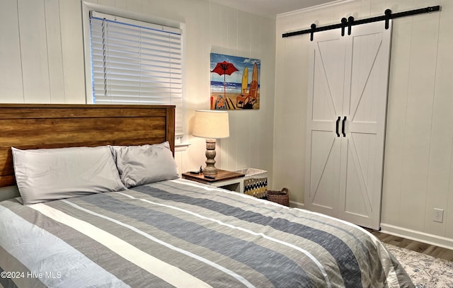 bedroom with hardwood / wood-style floors, a barn door, crown molding, and wooden walls