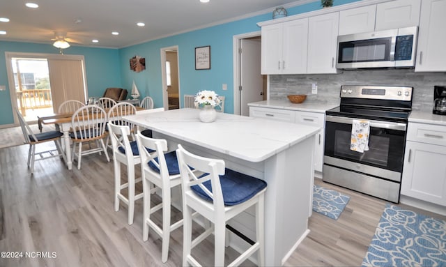 kitchen with ceiling fan, a kitchen breakfast bar, white cabinets, a kitchen island, and appliances with stainless steel finishes