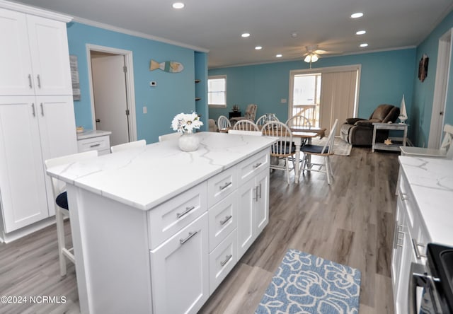 kitchen featuring white cabinetry, light stone countertops, ceiling fan, a kitchen breakfast bar, and light hardwood / wood-style floors