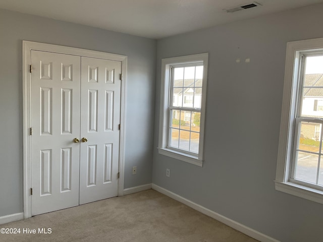 unfurnished bedroom featuring light carpet, a closet, and multiple windows