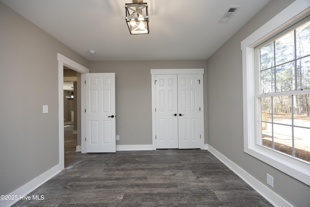 unfurnished bedroom with a closet, dark hardwood / wood-style flooring, and multiple windows