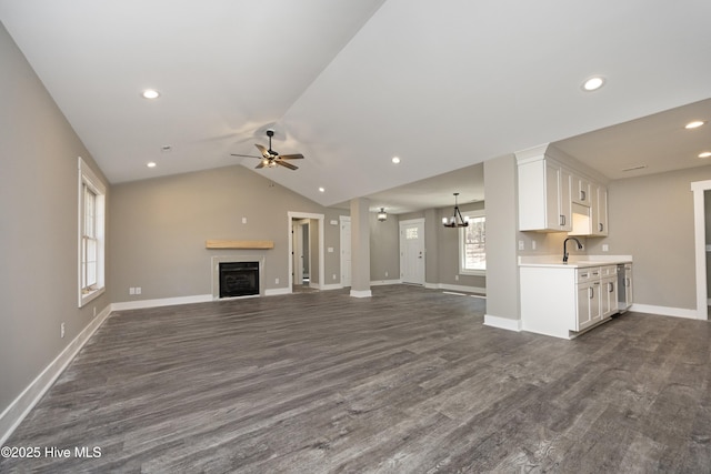 unfurnished living room featuring lofted ceiling, sink, ceiling fan with notable chandelier, and dark hardwood / wood-style flooring