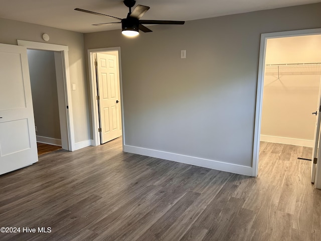 unfurnished bedroom with ceiling fan, wood-type flooring, a walk in closet, and a closet