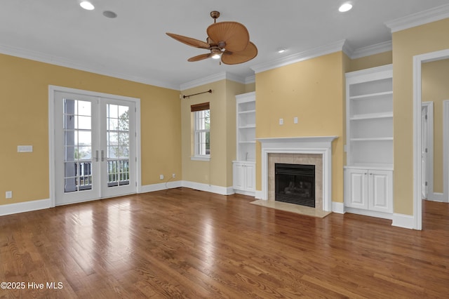 unfurnished living room featuring french doors, ceiling fan, built in features, ornamental molding, and a tiled fireplace