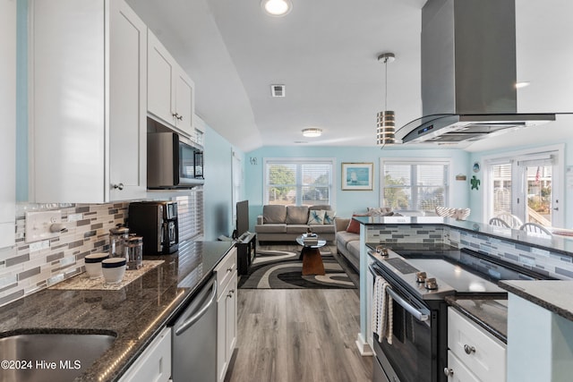 kitchen featuring decorative backsplash, appliances with stainless steel finishes, wall chimney range hood, decorative light fixtures, and white cabinets