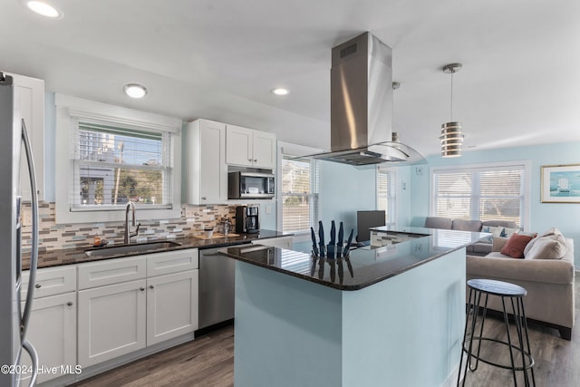 kitchen with sink, hanging light fixtures, a kitchen island, island range hood, and white cabinetry