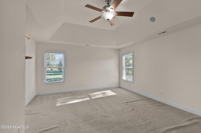 carpeted empty room with a raised ceiling, ceiling fan, and plenty of natural light