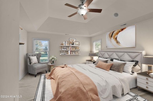 carpeted bedroom featuring a tray ceiling, multiple windows, and ceiling fan