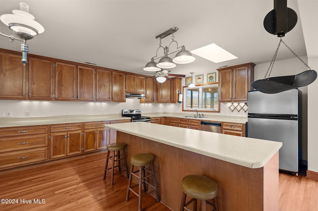 kitchen with appliances with stainless steel finishes, a kitchen breakfast bar, a skylight, sink, and light hardwood / wood-style flooring