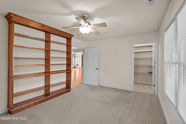 unfurnished bedroom with light carpet, a walk in closet, a textured ceiling, ceiling fan, and a closet