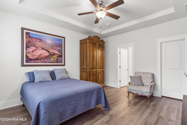 bedroom featuring a raised ceiling, ceiling fan, and wood-type flooring